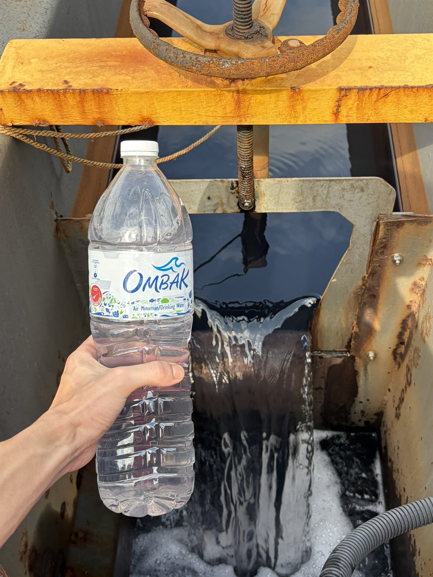 Treated discharge water held up next to a sealed drinking-water bottle — both visibly clear